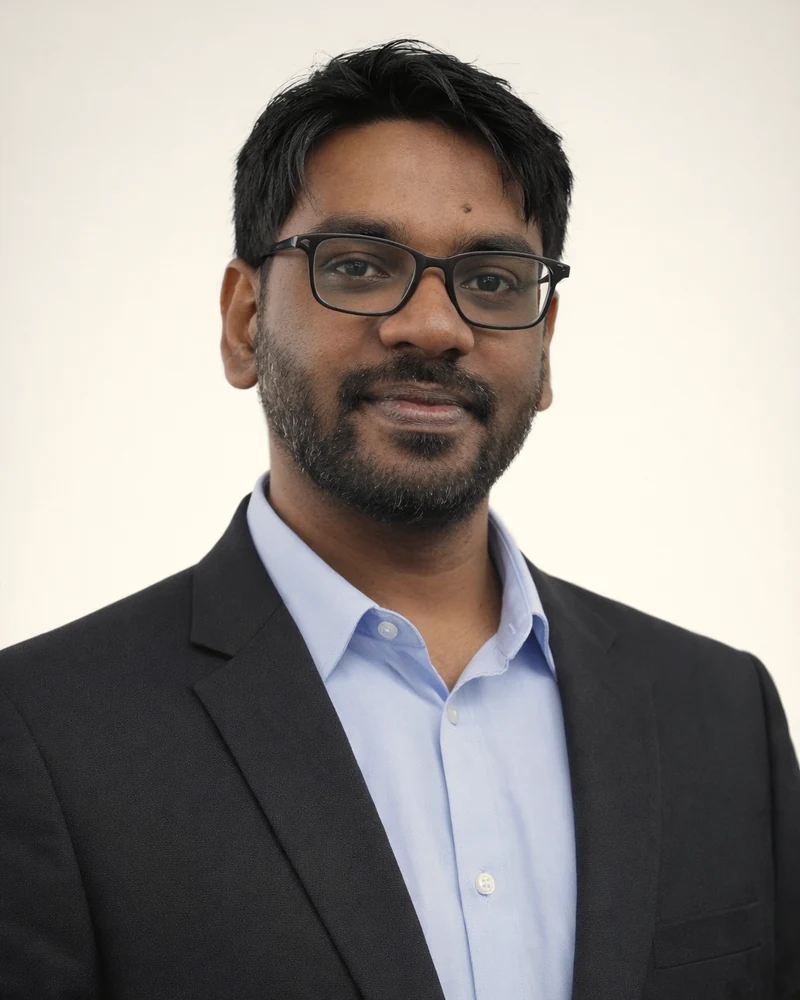 Sakhil Ahamed Ebrahim, wearing glasses and a dark suit over a light blue shirt.